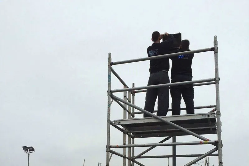 Two electricians on a scaffold tower working on a tall illuminated sign
